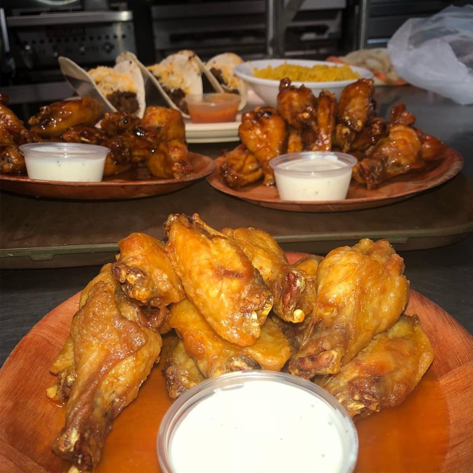 Plates of Rickey's Sports Bar & Grill chicken wings with dipping sauce, tacos, and rice.