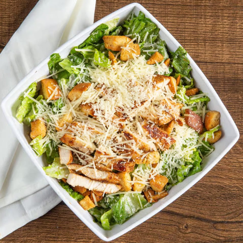 Overhead view of a Caesar salad with grilled chicken, croutons, and shredded Parmesan cheese.