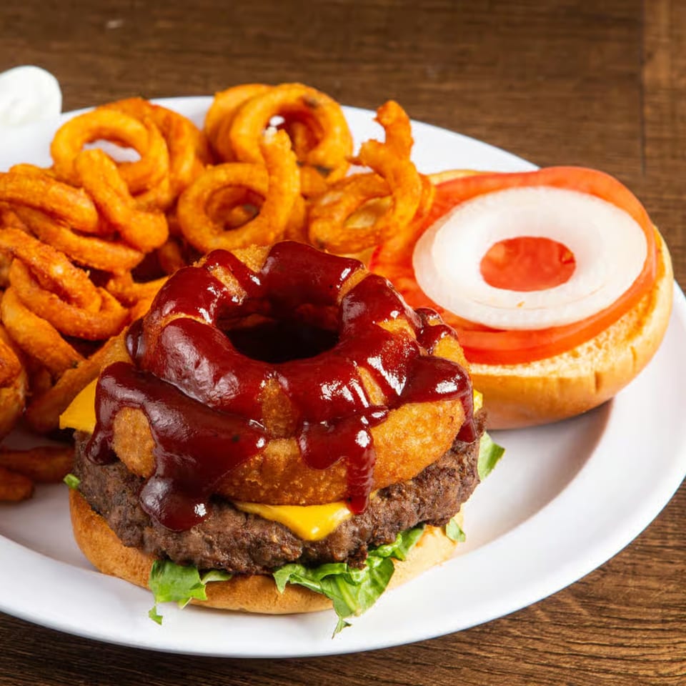Rickey's BBQ burger with onion rings, cheese, lettuce, and curly fries on a white plate.