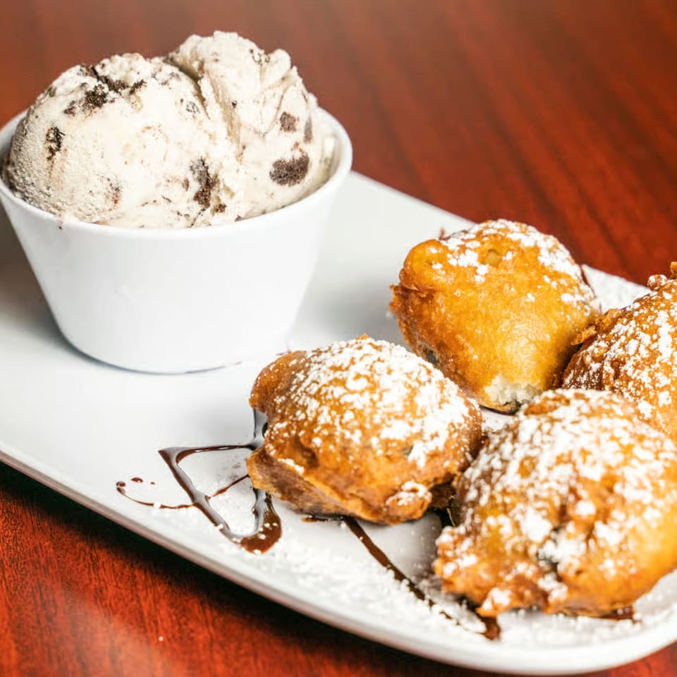A white bowl of cookies and cream ice cream next to four powdered sugar-dusted fried dough balls.